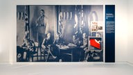 Foto mit Adolf Hitler und ein Schaukasten, in dem eine gefaltete Hakenkreuzfahne ist