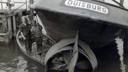 Drei Männer arbeiten an der Schraube eines Schiffs mit der Aufschrift 'Duisburg'