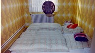 Schlafzimmer mit einer bunten Tapete und violetten Deckenlampe