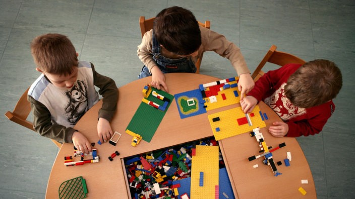 Drei Jungen spielen im Kindergarten Spielhaus an einem Tisch mit Legosteinen