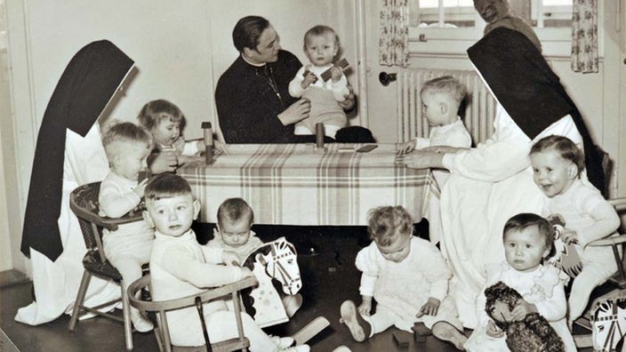 Ein Pater und zwei Nonnen mit Schützlingen in einem katholischen Kinderheim