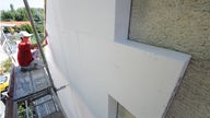 Bauarbeiter bringt Dämmplatten an einer Hauswand an