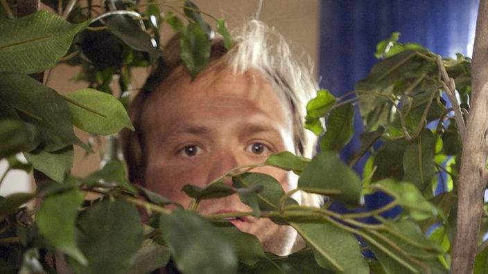 Ab ins Gebüsch, mein Hase! Klaus (Moritz A. Sachs) versteckt sich hinter der Grünpflanze, als Momo unangemeldet in die Wohnung kommt. Der soll nicht erfahren, dass Iffi und Klaus ein Paar sind.