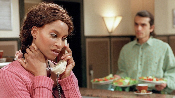 Mary (Liz Baffoe) telefoniert mit ihrem nigerianischen Ex-Geliebten - Vasily (Hermes Hodolides) lauscht misstrauisch.