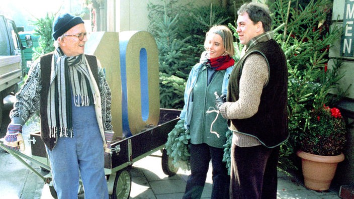 Olaf (Franz Rampelmann, rechts) und Valerie (Nadine Spruß) treffen auf der Straße auf einen Bauarbeiter (Friedrich Nowottny), der die Zahl 10 transportiert.
