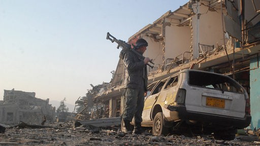 Kämpfer mit Waffe vor eine zerstörten Haus