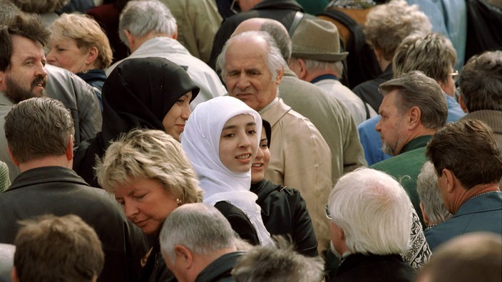 Frauen mit Kopftuch steht inmitten einer Menschenmenge