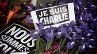 Schilder mit der Aufschrift Je suis Charlie und Blumen