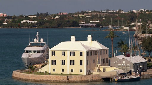 Ein Haus und eine Yacht am Meer, im Hintergrund weitere Häuser