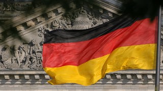 Die Deutschland-Fahne weht vor dem Reichstag in Berlin, auf dem der Spruch "Dem deutschen Volke" zu lesen ist. 