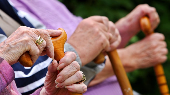 Hände älterer Menschen auf ihren Gehstöcken, Senioren auf einer Bank