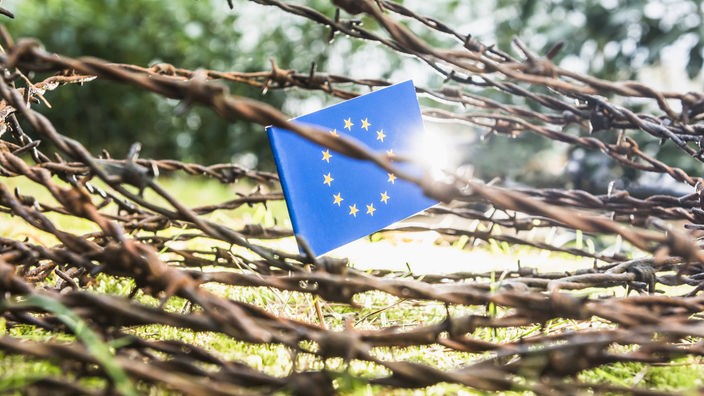Symbolbild für die Abgrenzung Europas: Flagge der Europäischen Union hinter Stacheldraht