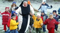 Nonne tobt mit Kindern im Schnee