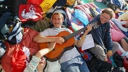Drei Jugendliche lachend und Gitarre spielend auf dem Weltjugendtag 2005
