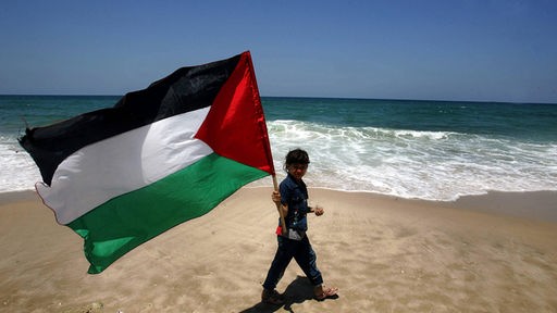 Junge läuft mit palästinensischer Fahne am Strand entlang