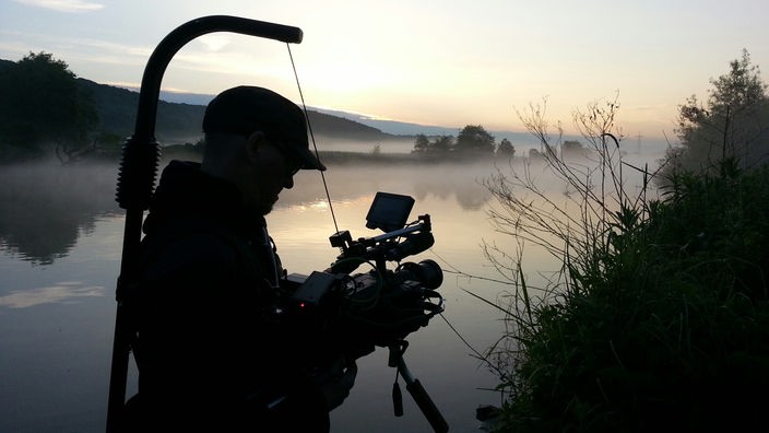 Mann im Morgengrauen mit Kameraausrüstung am Wasser