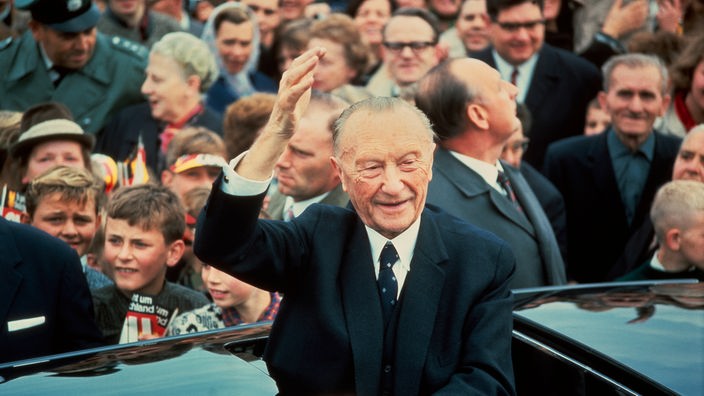 Konrad Adenauer winkend im offenen Wagen vor einer Menschenmenge