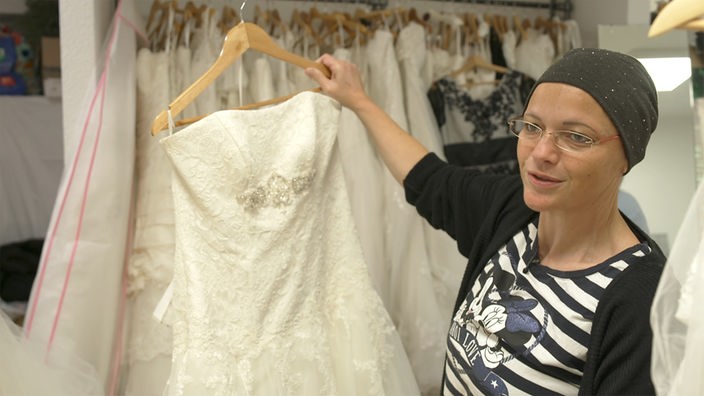 Frau hält weißes Hochzeitskleid in die Kamera