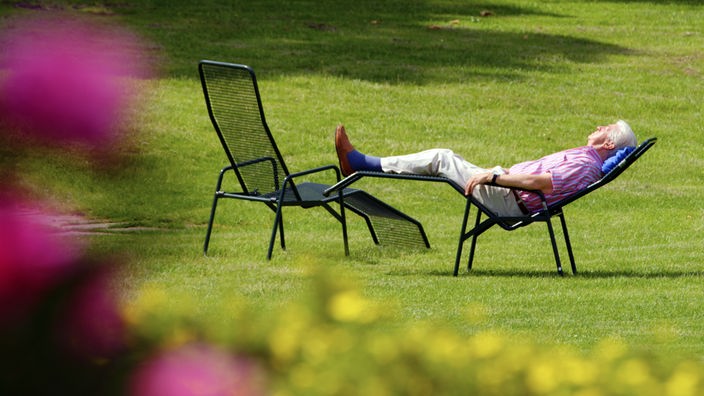 Ein Mann sonnt sitzt in einem Liegestuhl im Park und sonnt sich 