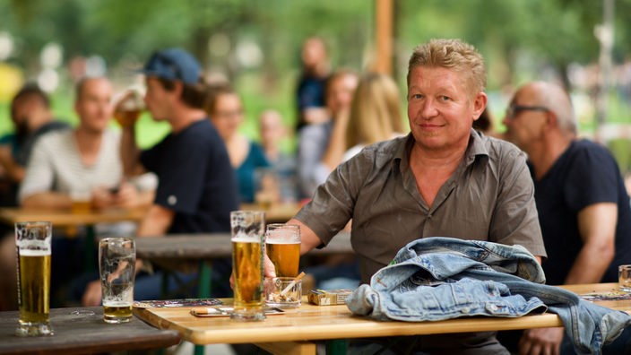 Ein Mann sitzt im Biergarten, lächelt in die Kamera