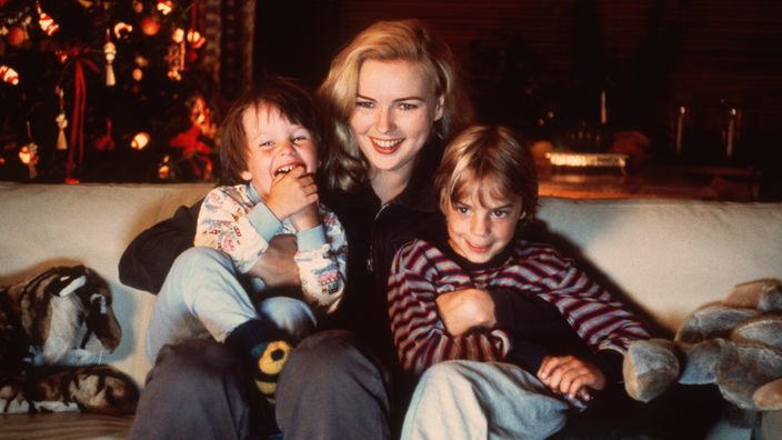 Foto aus dem Film: Veronika Ferres sitzt auf einem Sofa, zwei Kinder schmiegen sich an sie, alle lachen.