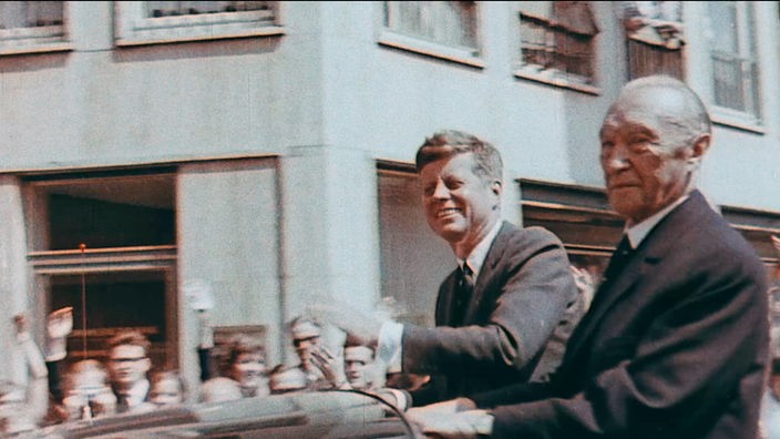John F. Kennedy und Konrad Adenauer fahren im offenen Wagen durch eine Menschenmenge