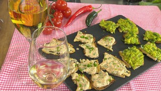 Crostini - Brote mit verschiedenen Belägen auf einer Platte serviert, daneben zwei Gläser Wein