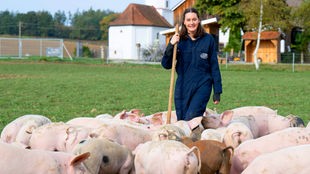 Katharina Mühlbauer auf der Weide umringt von Schweinen. 