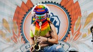 Saxophonspieler der Band Panteón Rococó trägt auf der Bühne eine bunte, gehäkelte Maske