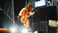 Bandmitglied mit freiem Oberkörper springt beim Gitarre spielen in die Luft