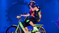 Ein Bandmitglied von Deichkind fährt im neongelben Fahrrad über die Bühne 
