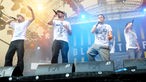 4 Jungs mit Mikrofon im weissen T-shirt nebeneinander auf der Bühne