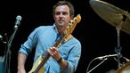 Bassist im hellblauen Hemd zwischen Mirkofon und Schlagzeug