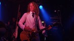 Ein Bandmitglied von Doomfoxx steht bei Bootleg im April 2006 mit weißem Hemd und Weste auf der Bühne und spielt Gitarre.