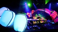 Leuchtende weiße Luftpolster vor der Bühne und leutende bunte Lichtbögen auf der Bühne, dazwischen ein Mitglied der Band Animal Collective.