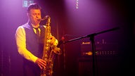 Saxophonist spielt im lila-gelben Licht der Scheinwerfer.