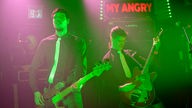 GItarrist und Bassist spielen nebeneinander im pink-grünen Scheinwerferlicht