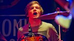 Schlagzeuger der Band "Palma Violets" spielt mit offenem Mund im lila Bühnenlicht