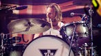 Mann mit längerem, blondem Haar sietzt vor einem Schlagzeug