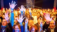 Die Menschen in der ersten Reihe des Publikums recken ihre Hände nach oben.