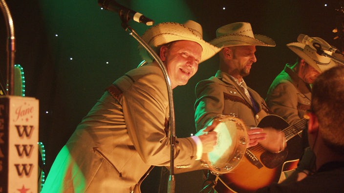 Olli Dittrich mit Tamburin dem Gitarristen von Texas Lightning mit lachendem Gesicht zugeneigt bei Bootleg im Oktober 2005