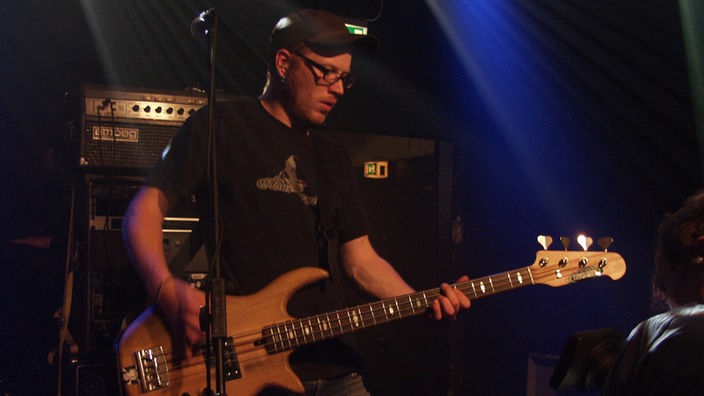 Alias Caylon Bassist mit spielt mit Kappe und Brille bei Bootleg im Oktober 2005