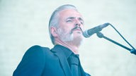 Mann mit grauem Haar und Bart am Mikrofon