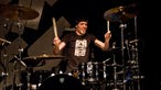 Der Drummer von Skip The Use mit schwarzem T-Shirt und schwarzer Kopfbedeckung zeigt vollen Einsatz an seinem schwarzen Drumkit.