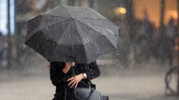Eine Frau steht mit Regenschirm in starkem Regen.