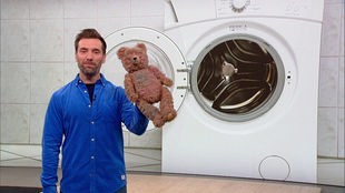 Das Bild yeigt Daniel Aßmann im Serviceyeit-Fernsehstudio. Im Hintergrund ist das Bild einer Waschmaschine zu sehen.