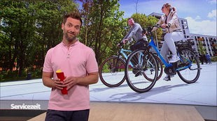 Der Moderator im SZ-Studio vor einem Bild vor zwei E-Bike-Fahrern