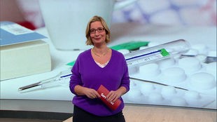 Das Bild zeigt Yvonne Willicks im Fernsehstudio. Im Hintergrund sieht man ein Fieberthermometer und Medikamente.