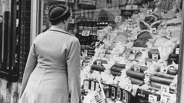 sw-Foto Eine Frau steht vor einem prall gefüllten Lebensmittelschaufenster (1949)