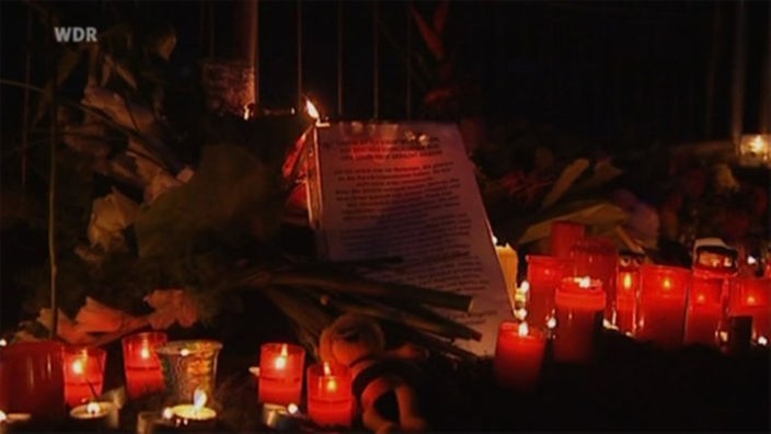 Bild eines Straßenaltars, der der Toten der Duisburger Loveparade gedenkt. Kerzen, Gedichte, Briefe, Blumen.